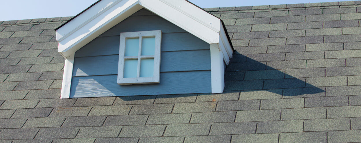 A close-up photograph of a residential home's roof. A small dutch dormer is in the center of the shot.